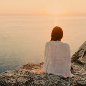 Remote Viewer Image a woman sat on the edge of a cliff, overlooking a sunset by the sea