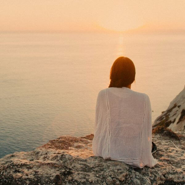 Remote Viewer Image a woman sat on the edge of a cliff, overlooking a sunset by the sea