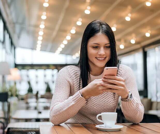 Woman texting a psychic reader in a coffee shop on a rose gold Phone